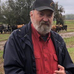 A man in red shirt and black hat standing next to cows.