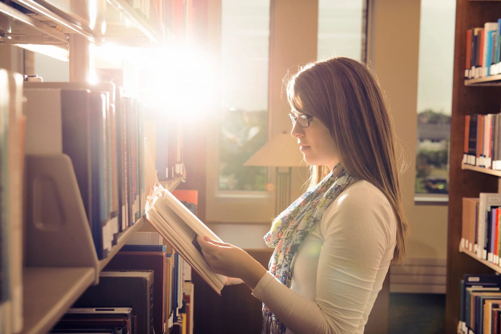 A woman reading in front of bookshelves.