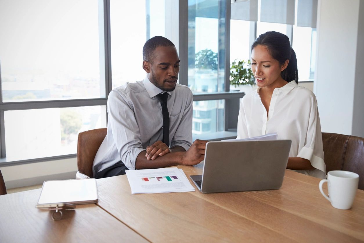 Two people sitting at a table looking at a laptop.